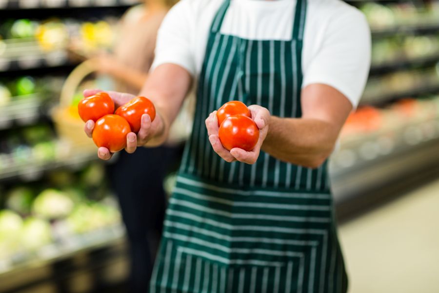 Arbeiter im Supermarkt mit ausgestreckten Armen und je einer Tomate in den Händen